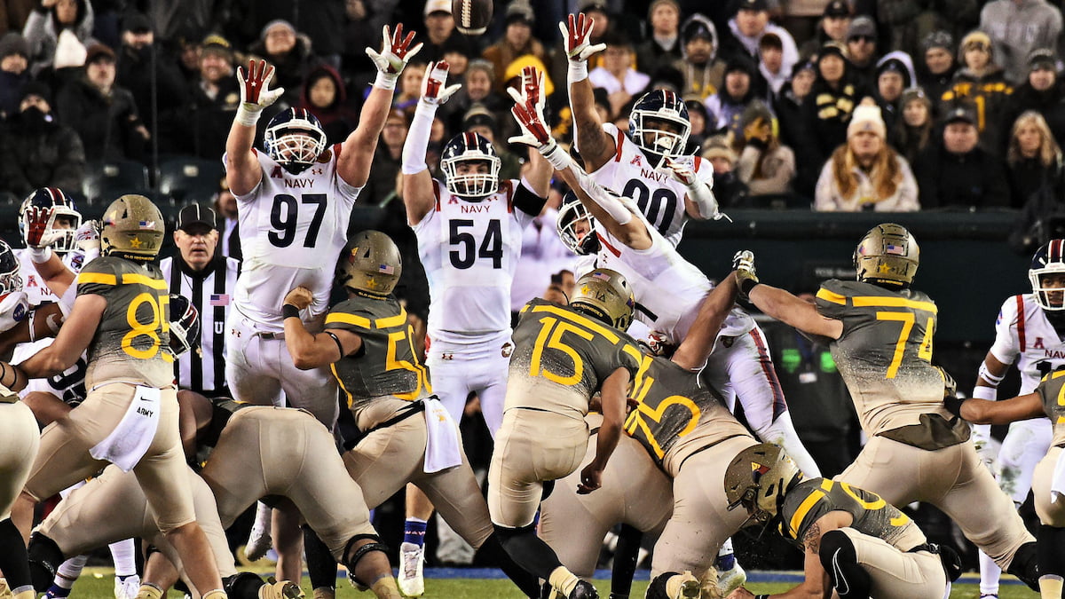 Navy college football players try to block the Army kicker's try.