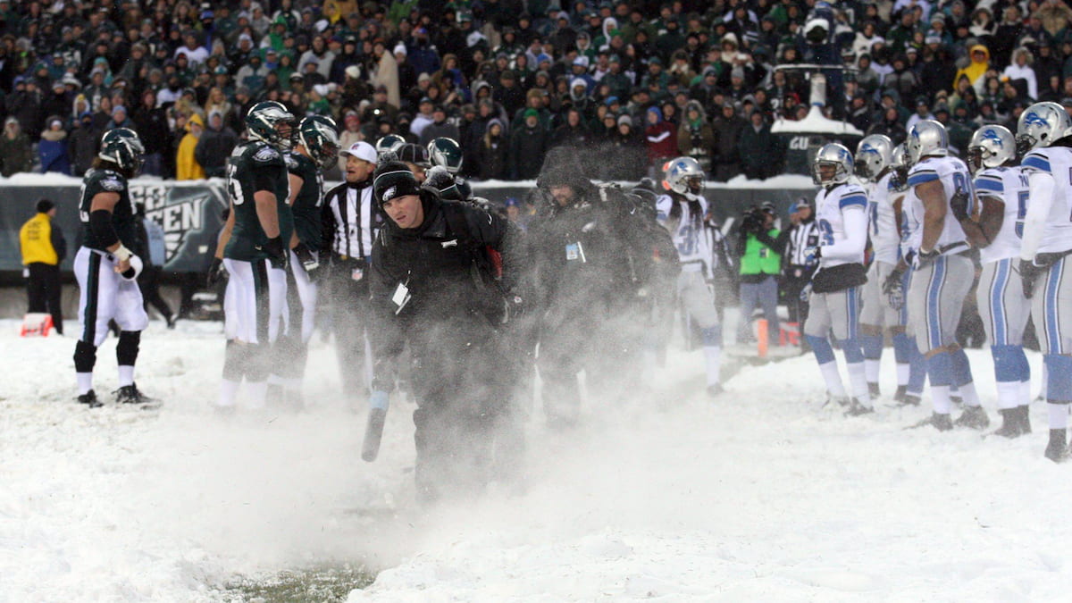 Ground staff clear snow from the ground during an NFL game.