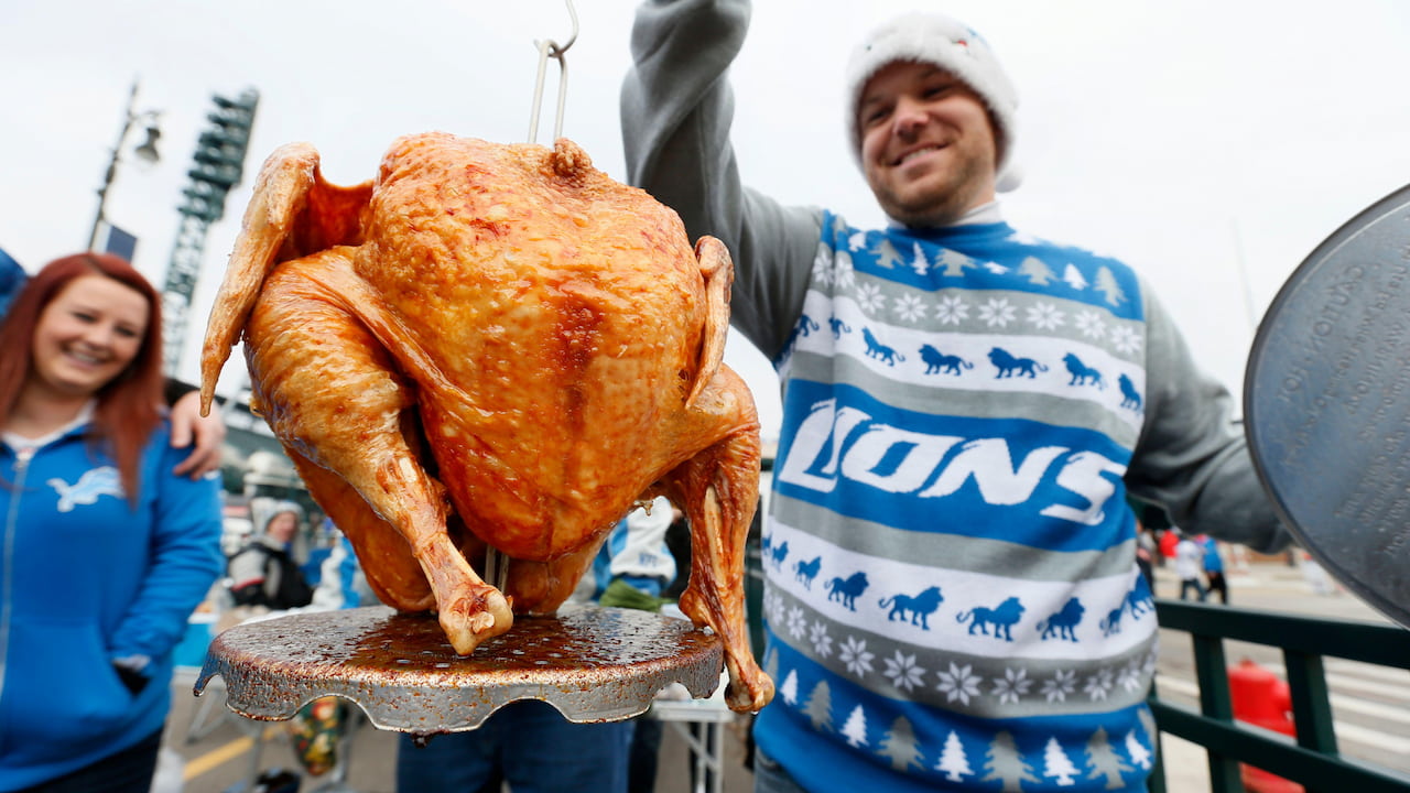 A fan in a Detroit Lions jumper holds up a turkey at Thanksgiving.