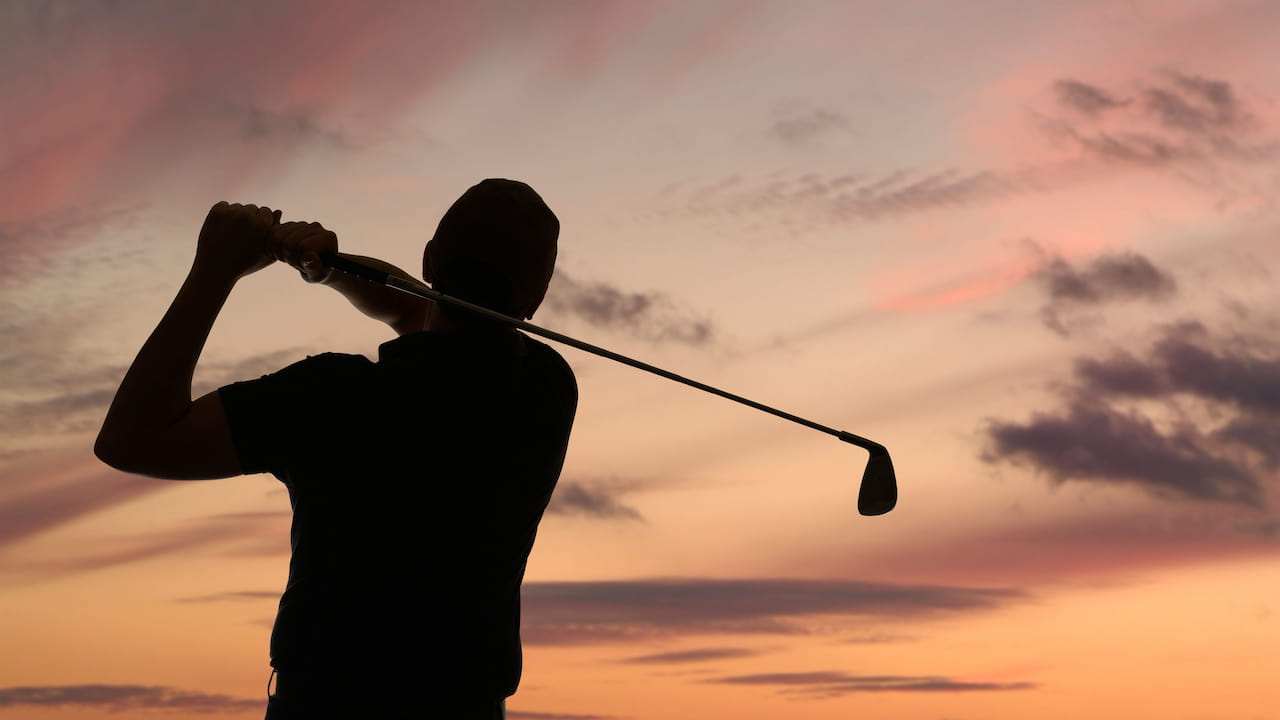 Silhouette of a golfer playing at dusk.