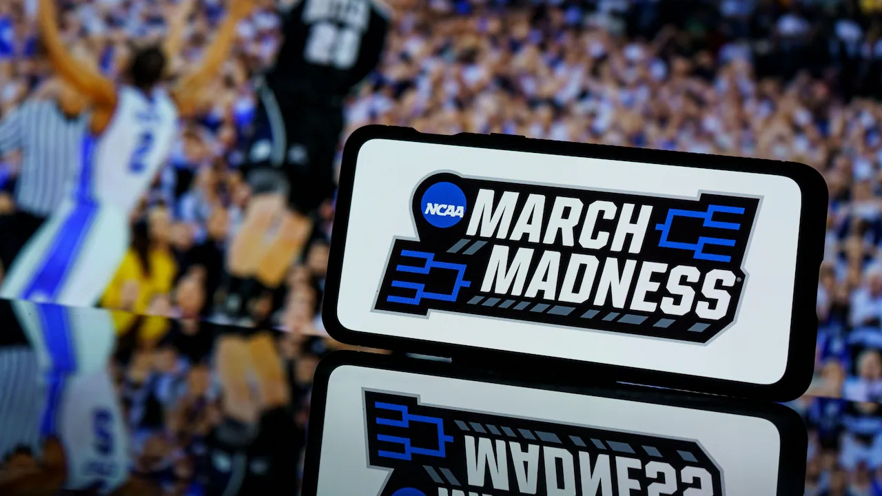 March Madness logo is displayed on a phone screen while the action of the NCAA Tournament unfolds.